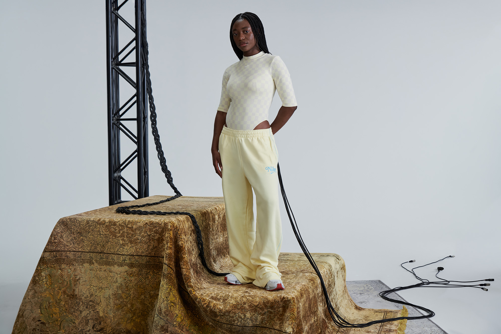 A woman stands next to a festival scaffolding equipment, with long wires flowing from her pockets