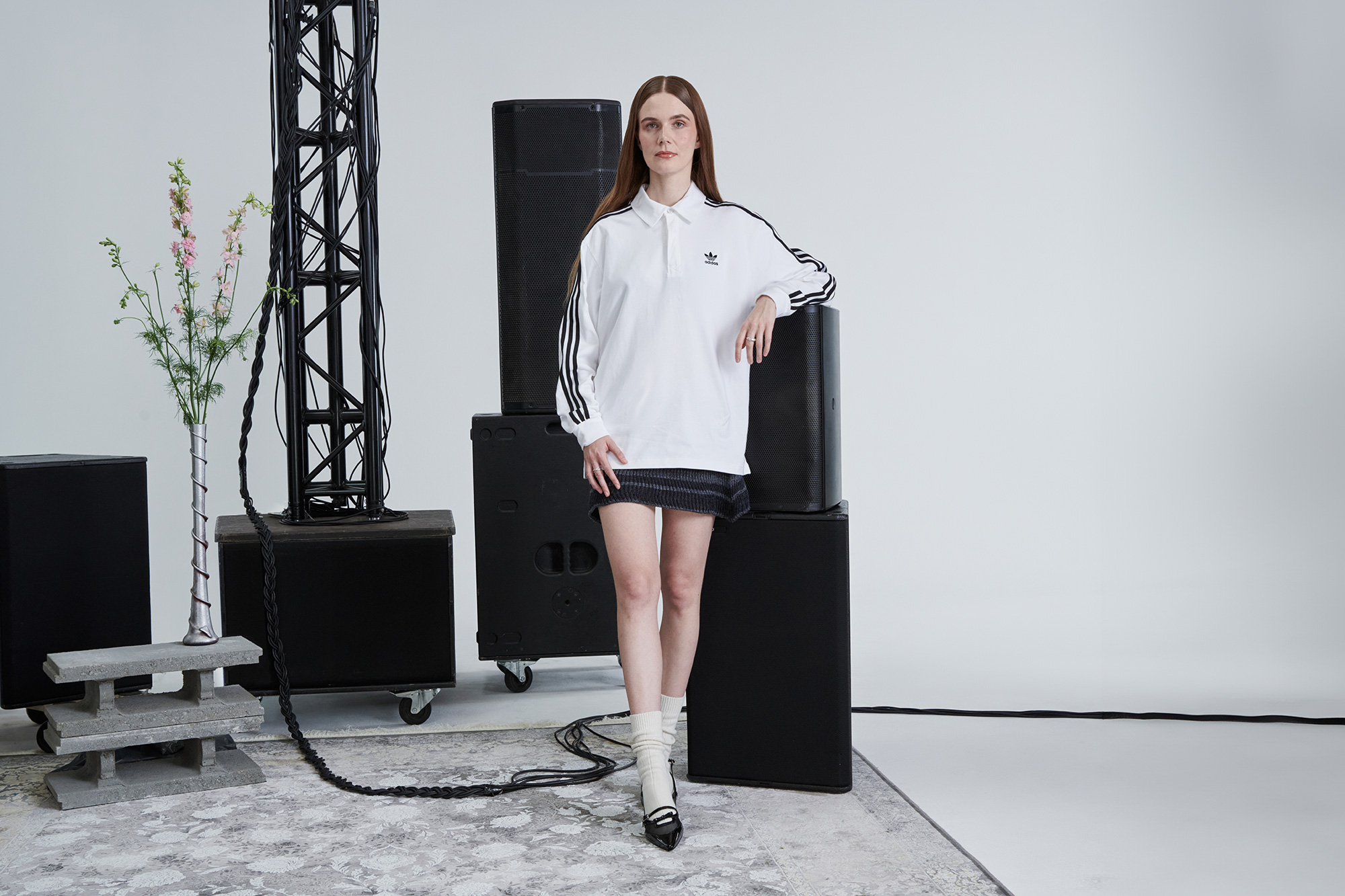 A woman leans against a large speaker in a grey coloured room